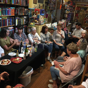 Participants of Barrel of Books and Games' monthly book club event sit in a circle inside the store talking next to a table with wine and snacks.
