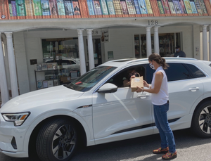 Barrel of Books and Games owner Crissy Stile delivers a curbside pickup order to a customer in a white car in front of the store.